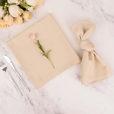 Beige napkin and tied napkin with flower on marble table setting.