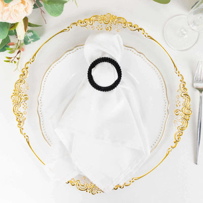 Black napkin ring on a white napkin atop an elegant gold-trimmed plate.