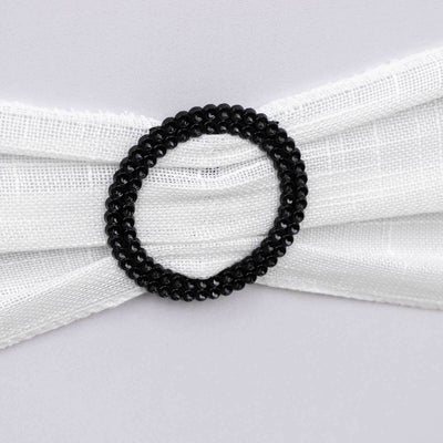 Black beaded circular ring on a white fabric background.