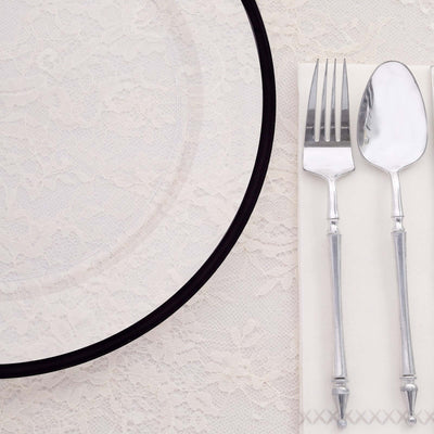 Elegant glass plate with silver fork and spoon on a lace tablecloth.