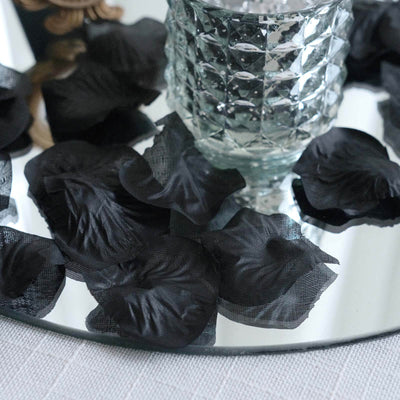 Black silk rose petals scattered on a mirrored surface with a decorative glass vase.