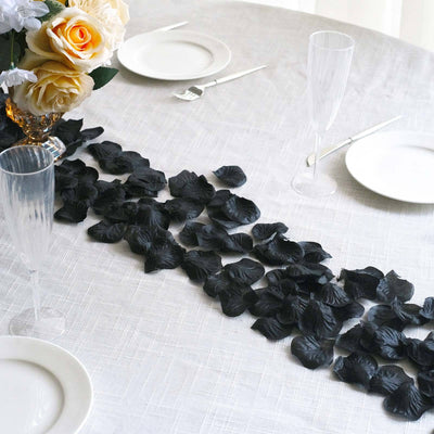 Black rose petals arranged elegantly on a table setting with plates and flutes.