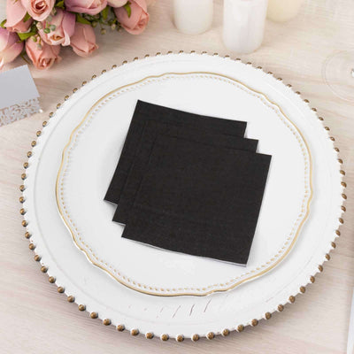 Black cocktail napkins stacked on an elegant plate with a floral backdrop.
