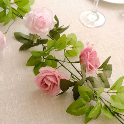 Pink artificial roses with green leaves on a table setting.