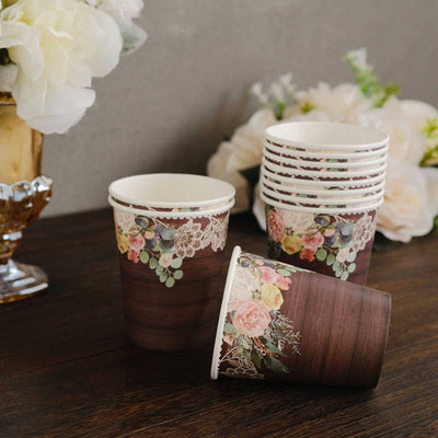 Floral paper cups stacked on a wooden table with decorative flowers in the background.