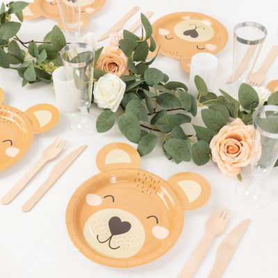 Bear-themed paper plates arranged with greenery and flowers for a party setting.