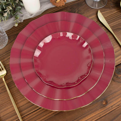 Elegant burgundy dinner plates stacked with gold trim on a rustic wooden table.
