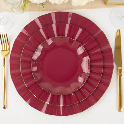 Set of three burgundy plates with gold trim on a table setting.