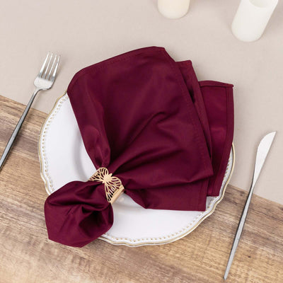 Burgundy napkin elegantly tied on a white plate with cutlery on a wooden table.