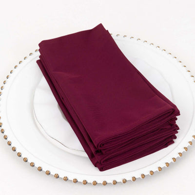 Burgundy fabric napkins neatly stacked on a decorative plate