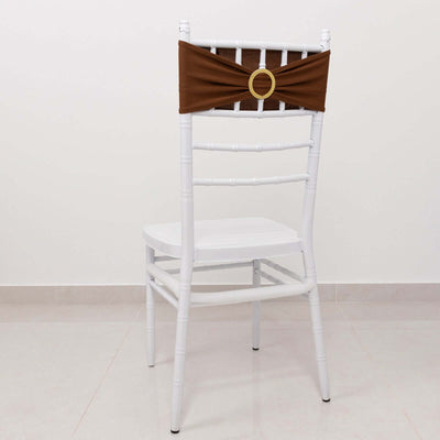 White chair with a brown fabric sash and gold ring decoration on a plain background.