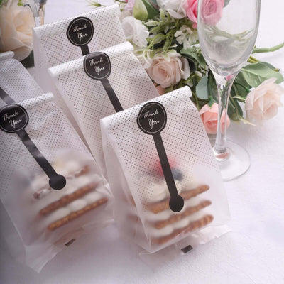 Delicate thank you gift bags with treats, styled with floral decor and a glass.