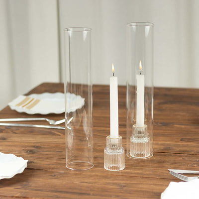 Clear glass candle holders with white candles on a wooden table.