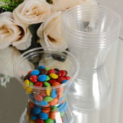 Clear plastic cups filled with colorful candies on a reflective surface.
