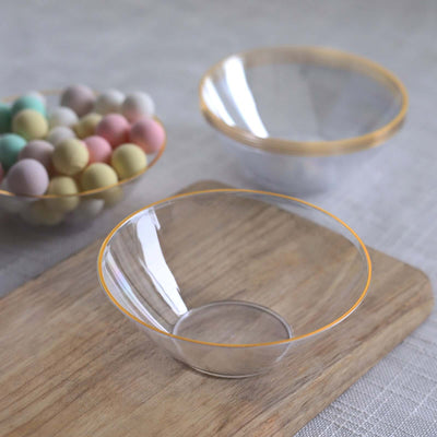 Clear bowls with gold rims on a wooden surface, with colorful candies in the background.