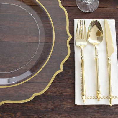 Elegant clear charger plate with gold trim and gold cutlery on a wooden table.