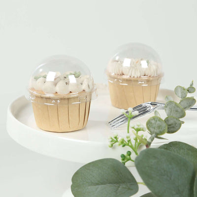 Two frosted cupcakes in clear dome containers on a white plate with greenery.