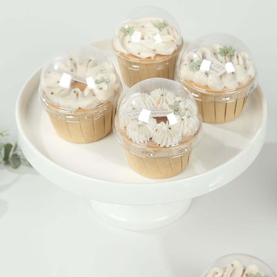 Assorted cupcakes with decorative frosting in clear domes on a white cake stand.