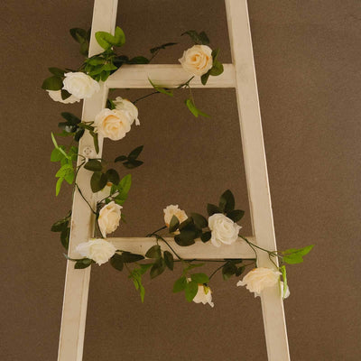 White ladder adorned with faux roses and green leaves.