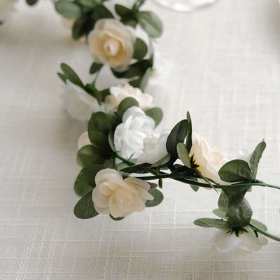 Artificial flower garland with white and cream blooms and green leaves.
