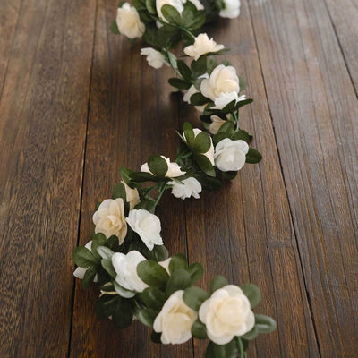 Artificial flower garland with white blooms and green leaves on wooden surface.