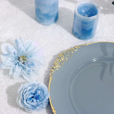 Elegant gray plate with gold trim, blue candles, and flowers on a textured white background.