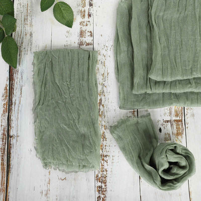 Green crinkled fabric laid out on wooden surface with leaves.