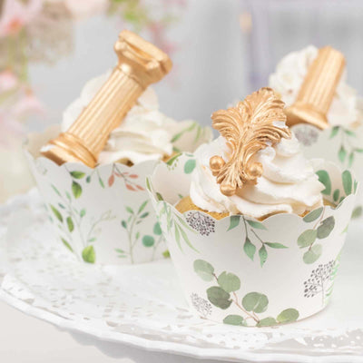 Decorative cupcakes with ornate toppers in floral cups on a platter.