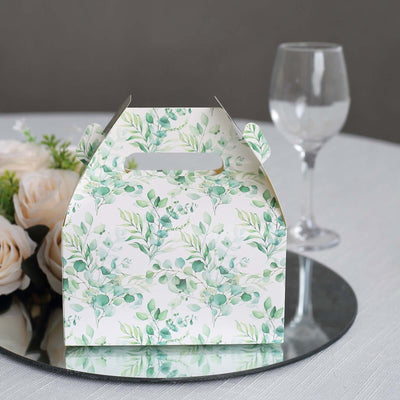 Floral-patterned gift box on a table with glasses and flowers in the background.