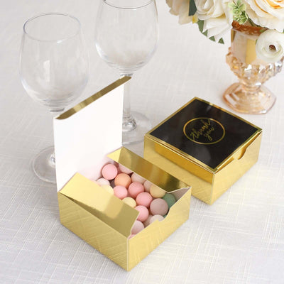 Gold gift box filled with pastel candies, placed beside two wine glasses.