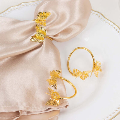 Gold butterfly napkin rings and bracelet on satin fabric.