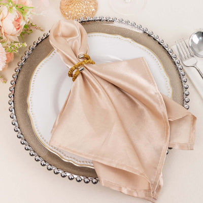 Elegant beige satin napkin tied with a gold ring on a decorative plate.