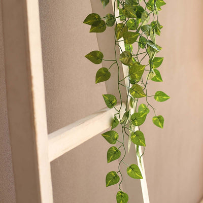 Artificial green vine with leaves cascading from a wooden ladder.