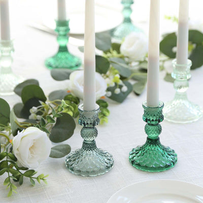 Green glass candle holders with white candles and floral accents on a table setting.
