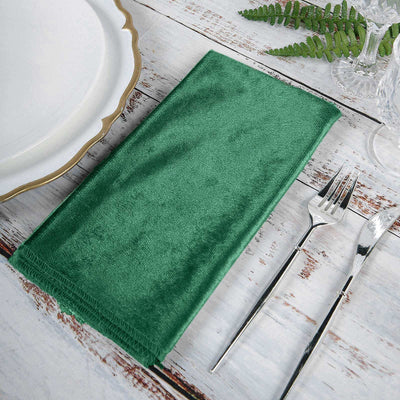 Green velvet napkin on rustic table setting with cutlery.