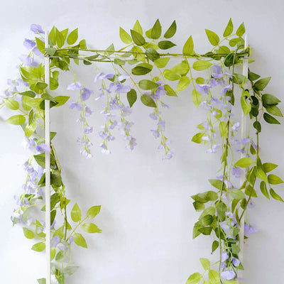 Artificial wisteria vine with green leaves and purple flowers on a white backdrop