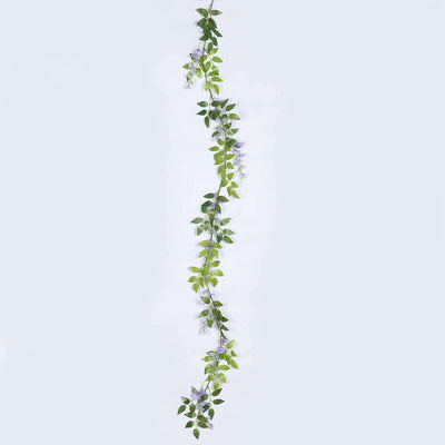 Artificial green leaf garland with purple flowers on a plain background