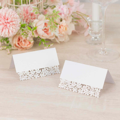 Elegant white place cards with floral cutout design on a light wooden table.