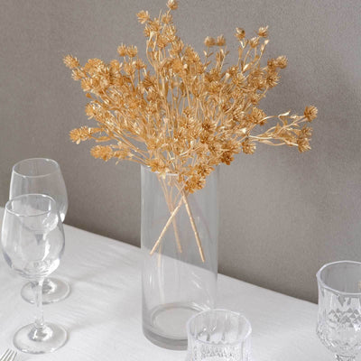Gold dried flowers in a clear vase on a table setting.