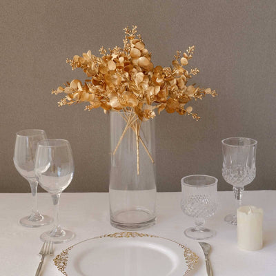 Gold dried flower arrangement in clear vase on elegant dining table setting.