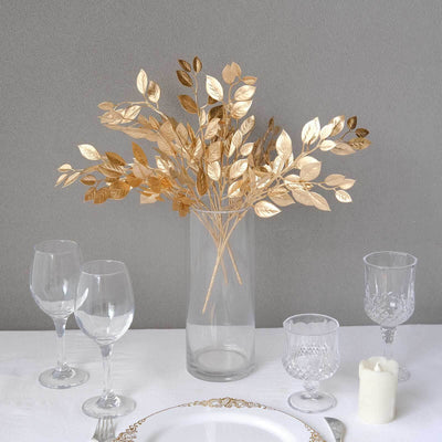 Gold leaf arrangement in a glass vase with elegant tableware.
