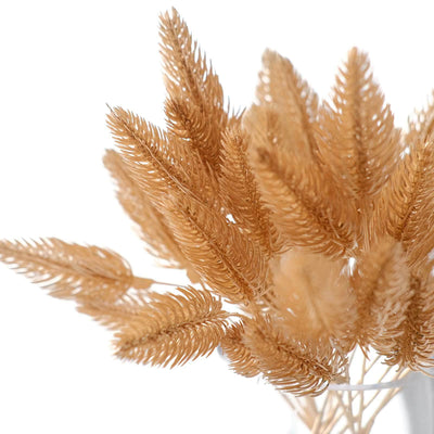 Dried golden foliage in a clear vase against a white background