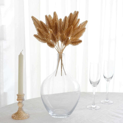 Clear glass vase with dried golden flowers, candle, and glasses on a table.