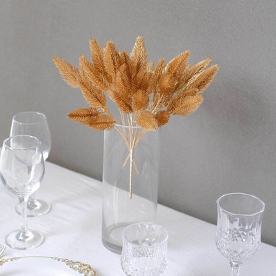 Dried golden grass in a clear vase on a table setting with glassware.