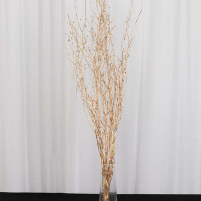 Gold decorative branches in a glass vase on a neutral background.