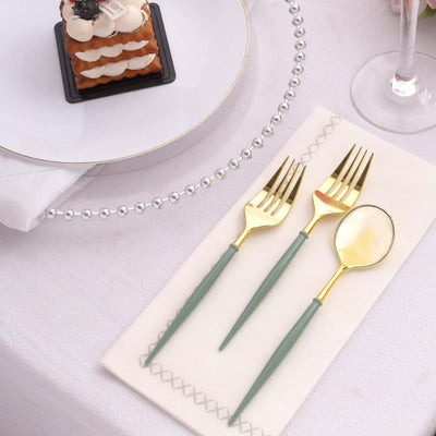 Elegant gold and green cutlery set on a napkin with a dessert plate in the background.