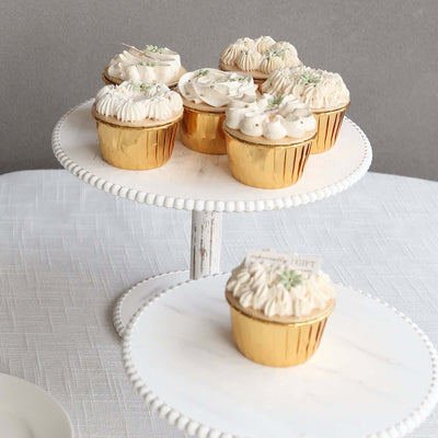 Elegant gold cupcake holders topped with creamy frosting on a cake stand.