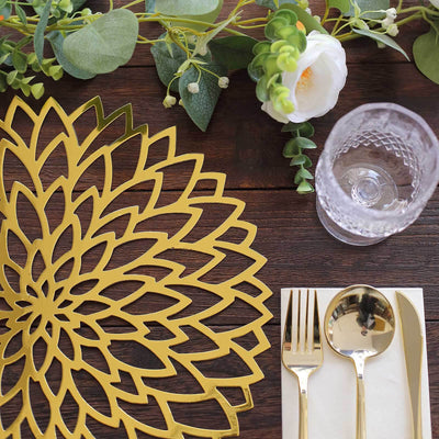 Gold floral placemat on a wooden table with cutlery and greenery decor.