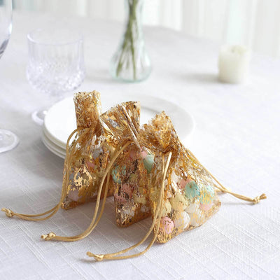 Gold organza bags filled with colorful candies on a white tablecloth.