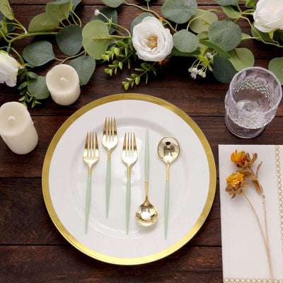 Elegant gold and mint cutlery set on a decorative plate with greenery and candles.